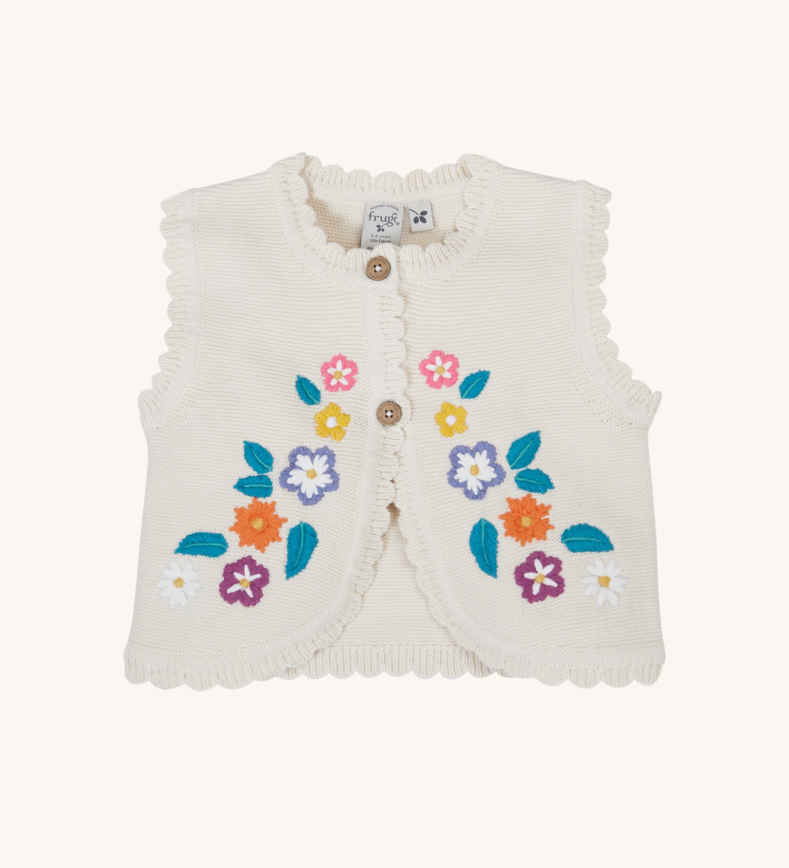 Frugi Oatmeal Flowers Connie Cotton Knitted Sleeveless Cardigan. This white oatmeal sleeveless cardigan has cute scalloped edges and is decorated with pretty embroidered flowers and leaves on the front.