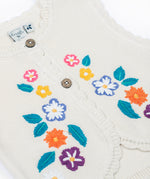 A close up of the embroidered flowers on the front of the Frugi Oatmeal Flowers Connie Cotton Knitted Sleeveless Cardigan. This white oatmeal sleeveless cardigan has cute scalloped edges and is decorated with pretty embroidered flowers and leaves on the front.  This waistcoat is a part of a wide range of organic cotton clothing for children available here at Babipur.