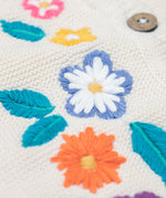A close up of one of the embroidered flowers on the front of the Frugi Oatmeal Flowers Connie Cotton Knitted Sleeveless Cardigan. This white oatmeal sleeveless cardigan has cute scalloped edges and is decorated with pretty embroidered flowers and leaves on the front.  This waistcoat is a part of a wide range of organic cotton clothing for children available here at Babipur.