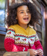 A child wearing the Frugi Festive Fair Isle Organic Cotton Kids' Carol Cardigan featuring red, yellow and green patterns and robin redbreast details. 
This knitted cardigan is a part of a wide range of organic cotton clothing for children available here at Babipur.