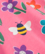 A close up of the print detail on the Frugi Sofia skater dress with a fun flowers design on a tulip pink background.