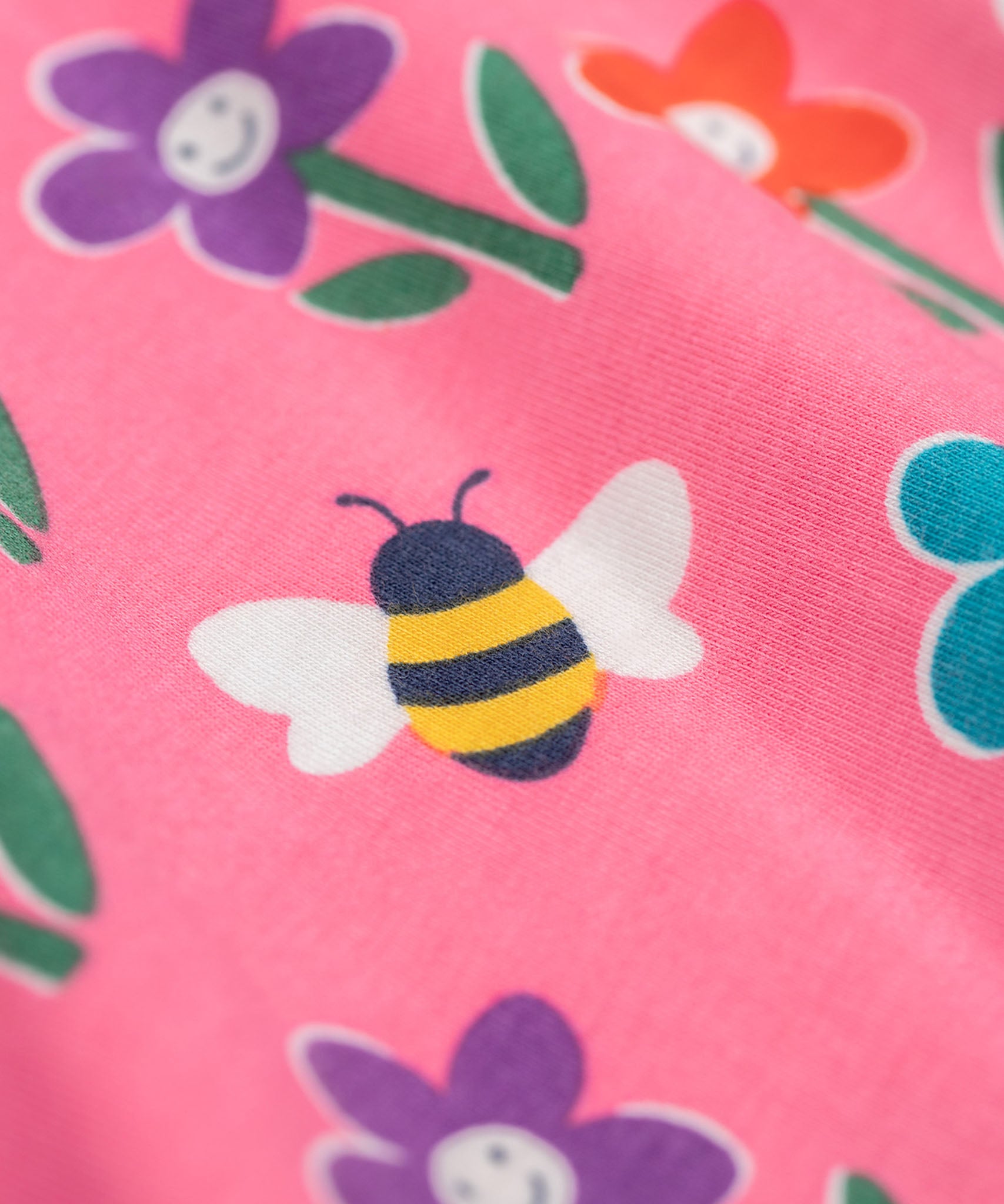 A close up of the print detail on the Frugi Sofia skater dress with a fun flowers design on a tulip pink background.
