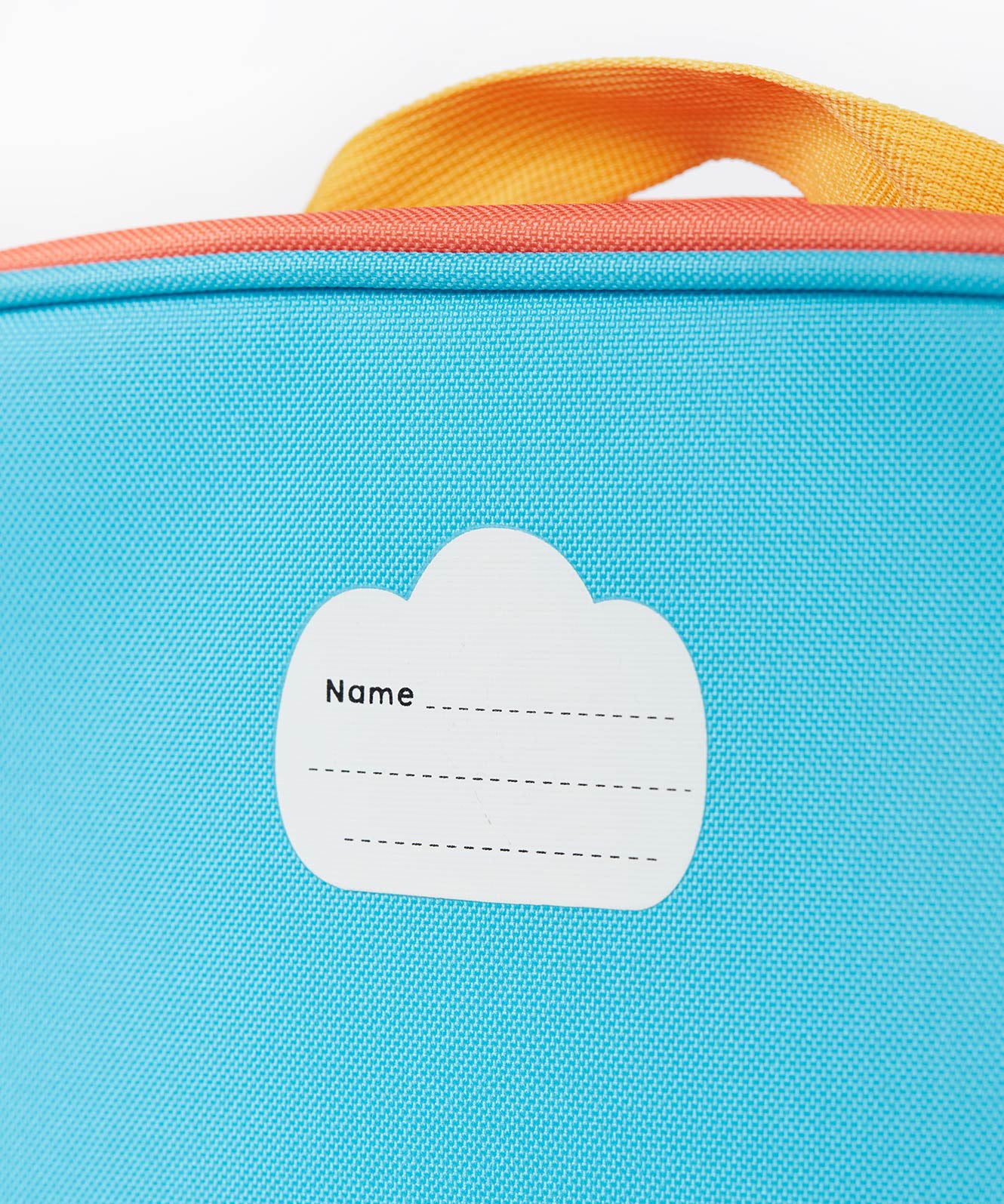 A close up of the Frugi kids pack a lunch bag in rainbow sun. Showing the name tag patch detail and yellow carry handle detail