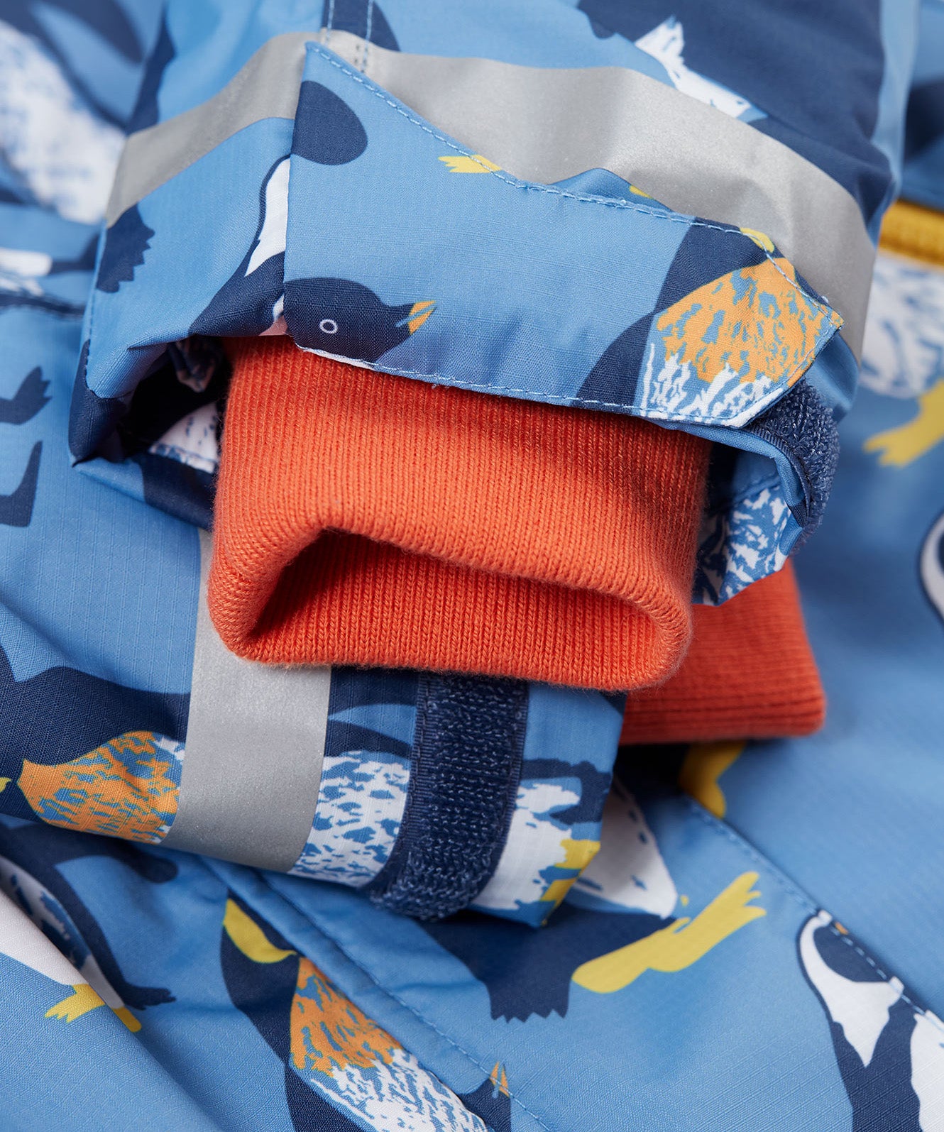 A close up of the Frugi kids snow and ski coat in penguin waddle showing the orange storm cuff detail and reflective strips