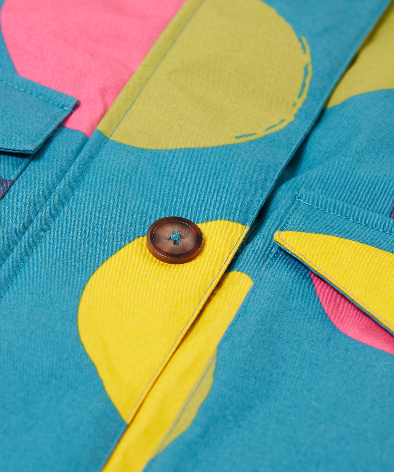 A close up of the Frugi khaki super spot  parka showing the button fastener and pocket detail on light blue organic cotton fabric