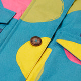 A close up of the Frugi khaki super spot  parka showing the button fastener and pocket detail on light blue organic cotton fabric