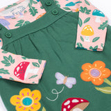 A close up of the Frugi kids pippa holly green fun guys pinafore outfit showing the woodland inspired prints detail and button fasteners on the pinafore on organic cotton fabric.