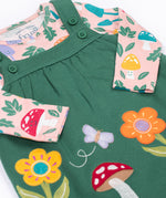 A close up of the Frugi kids pippa holly green fun guys pinafore outfit showing the woodland inspired prints detail and button fasteners on the pinafore on organic cotton fabric.