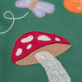 A close up of the Frugi kids pippa holly green fun guys pinafore outfit showing the mushroom applique detail on green organic cotton fabric.