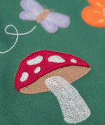 A close up of the Frugi kids pippa holly green fun guys pinafore outfit showing the mushroom applique detail on green organic cotton fabric.