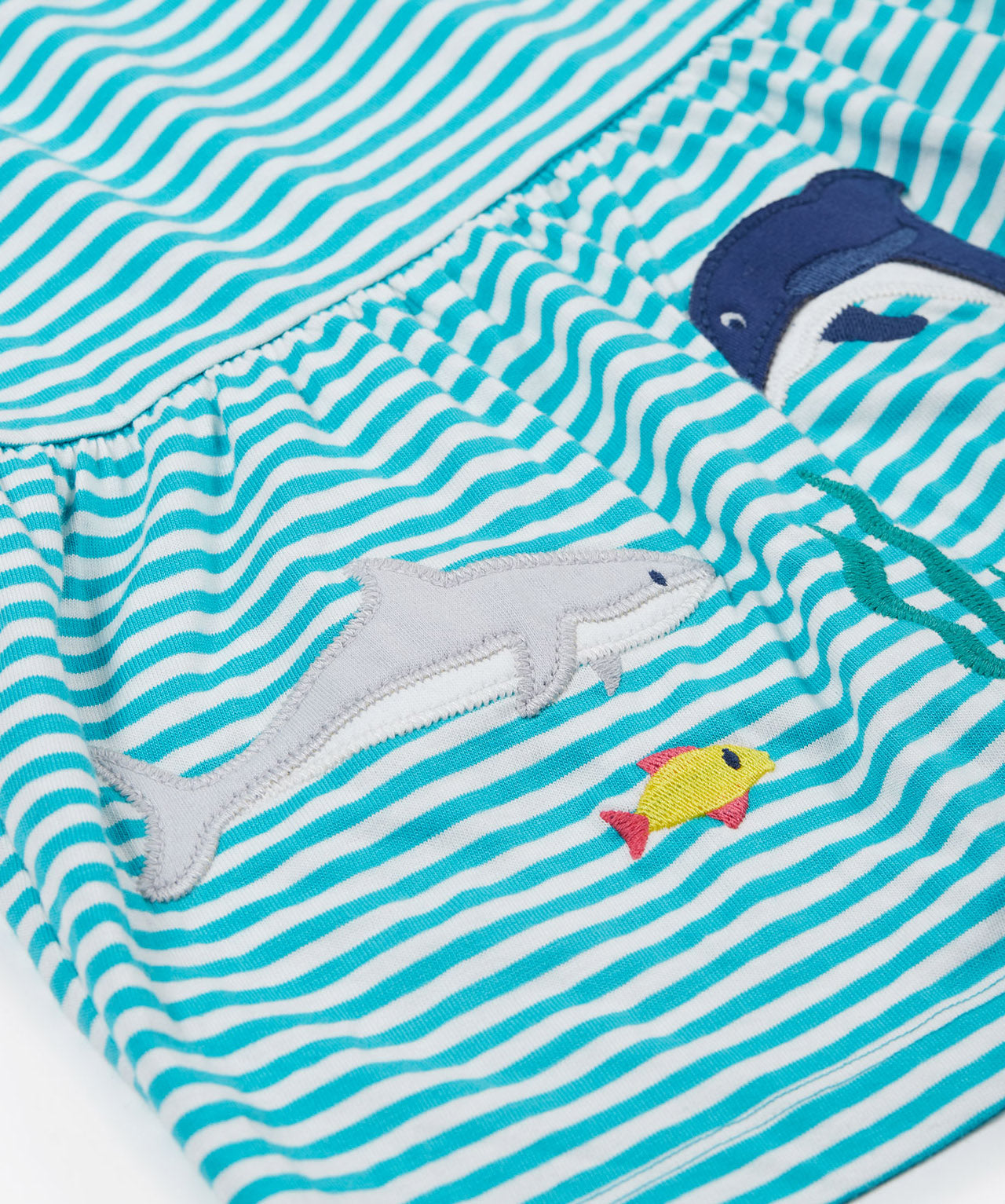 A close up of Frugi Pixy Sea Moss Mini Stripe Dress, with a Sealife print along the bottom, featuring a shark, a dolphin and a small fish.