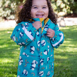 A toddler standing outside and wearing the Frugi puddle buster panda play coat.   light blue waterproof hooded coat with playful prints of pandas and rainbows with yellow zip trim