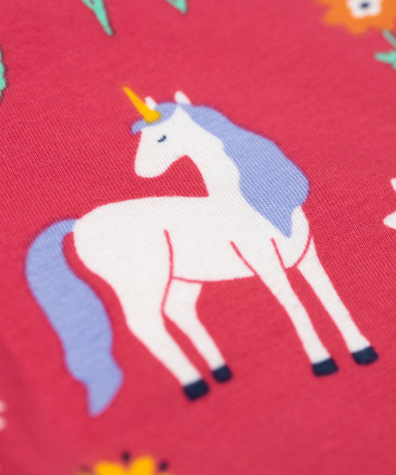 A close up of a unicorn on the leggings of the Frugi grape purple unicorn Organic Cotton Ottlie Outfit. An outfit with a purple coloured top with a unicorn applique on the front and pink unicorn print leggings. This outfit is a part of a wide range of organic cotton clothing for children available here at Babipur.