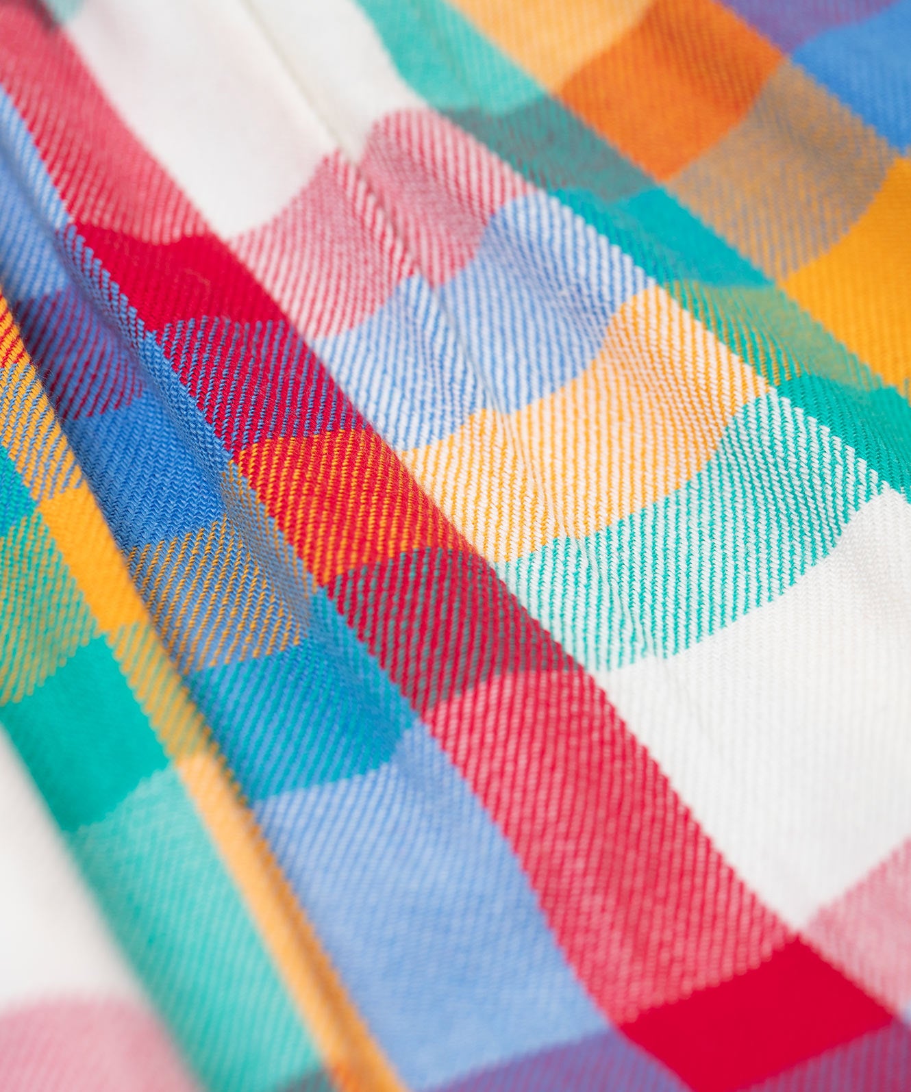 A close up of the multicoloured material of the Frugi Rainbow Check Organic Cotton Ffion Dress. The dress has a rounded collar details and button closure on the front. This festive kids dress is a part of a wide range of organic cotton clothing for children available here at Babipur.