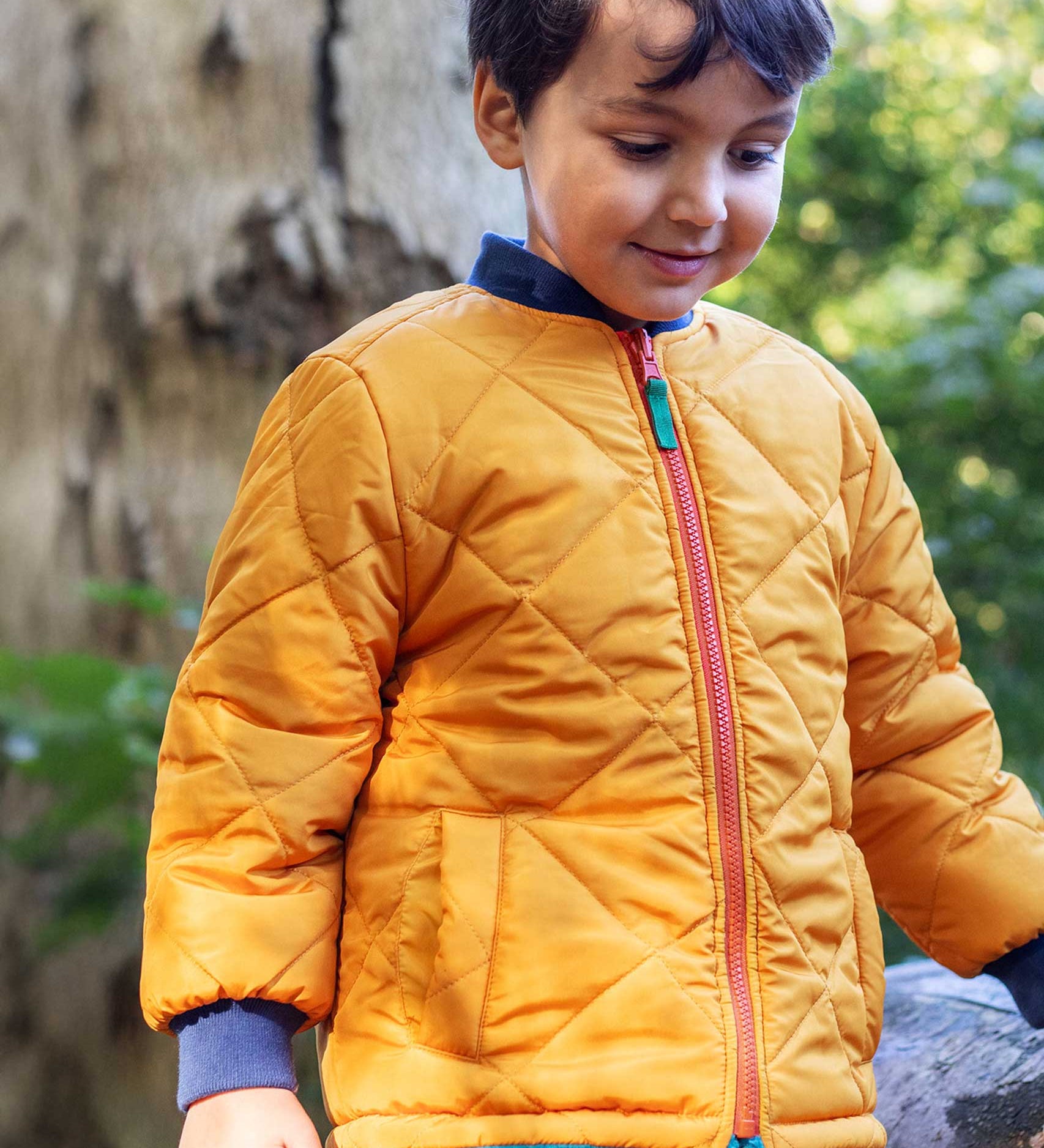 A child wearing the Frugi robin reversible quilted jacket in yellow gold with boat blue fleece.