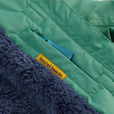 A close up of the Frugi kids snow and ski coat in green with a mountain scene print. Showing the thick navy fleece inner and a secret snack pocket on the inside