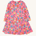 The Frugi Sofia skater dress with a fun flowers design on a tulip pink background. The dress has long sleeves.