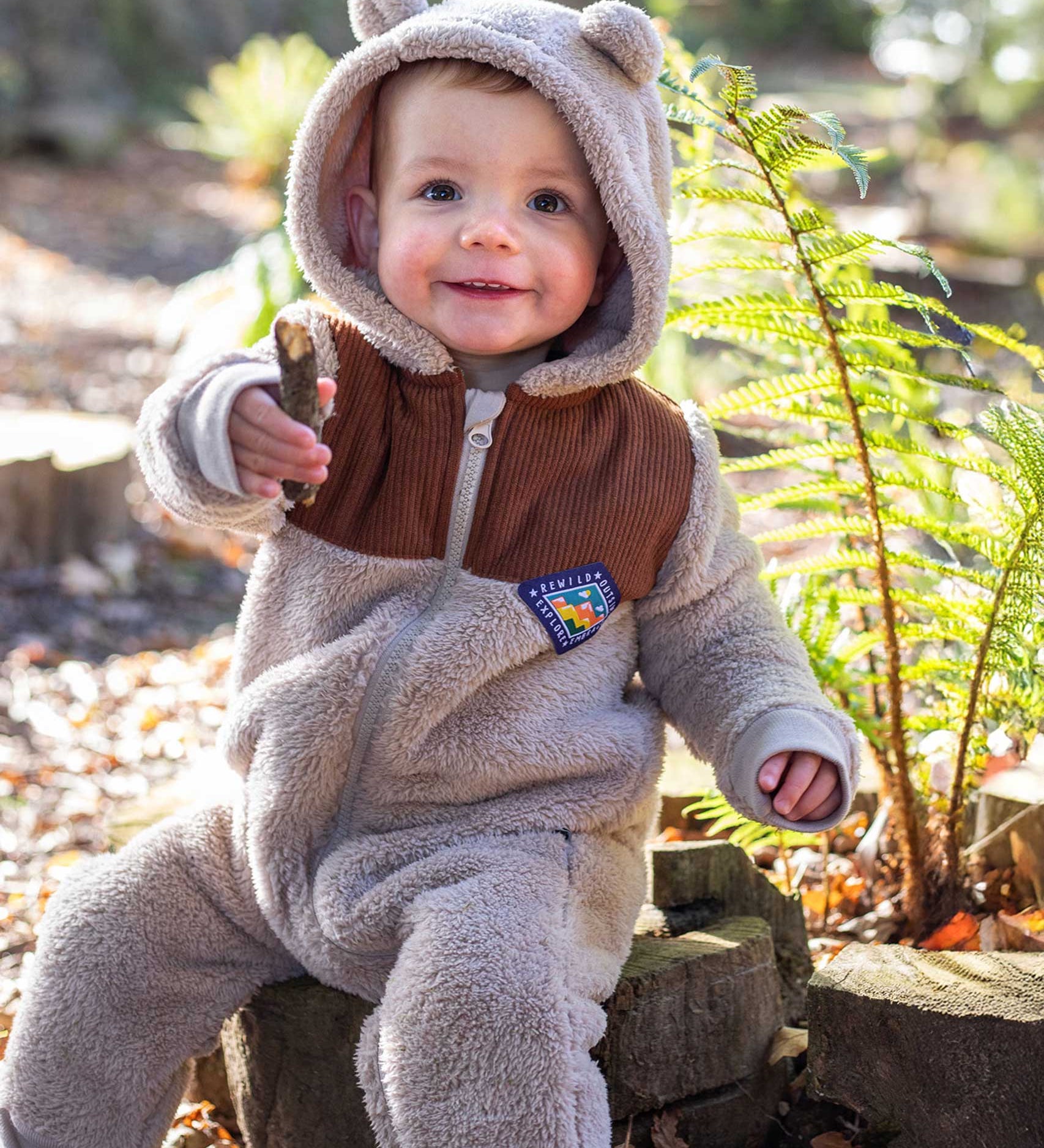 A child sitting on a log wearing the Frugi Cord ted fleecy snuggle suit .
