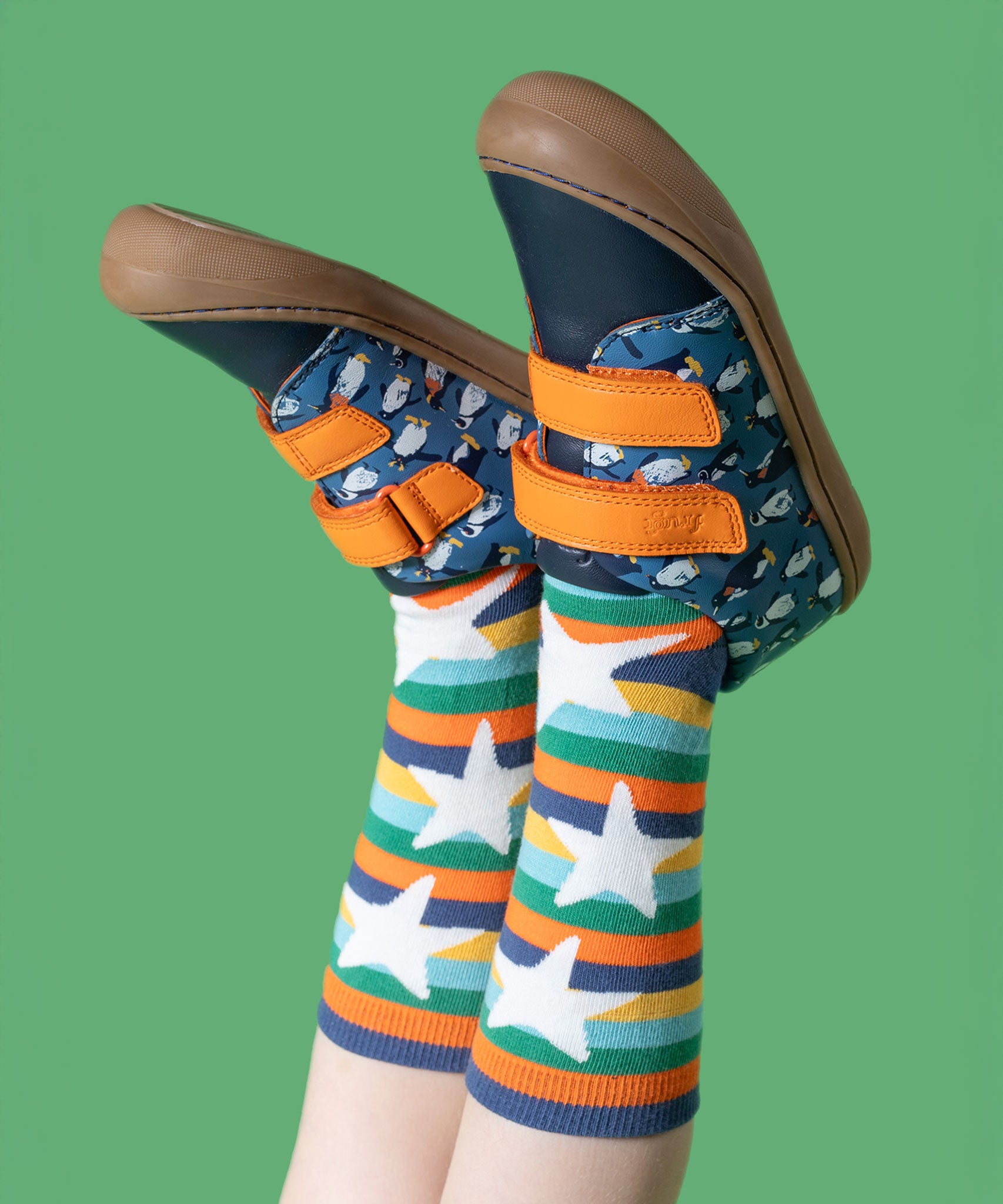 A child wearing the Frugi Penguin Print Tide Low Top velcro closure leather children's shoes with Frugi rainbow striped star socks.