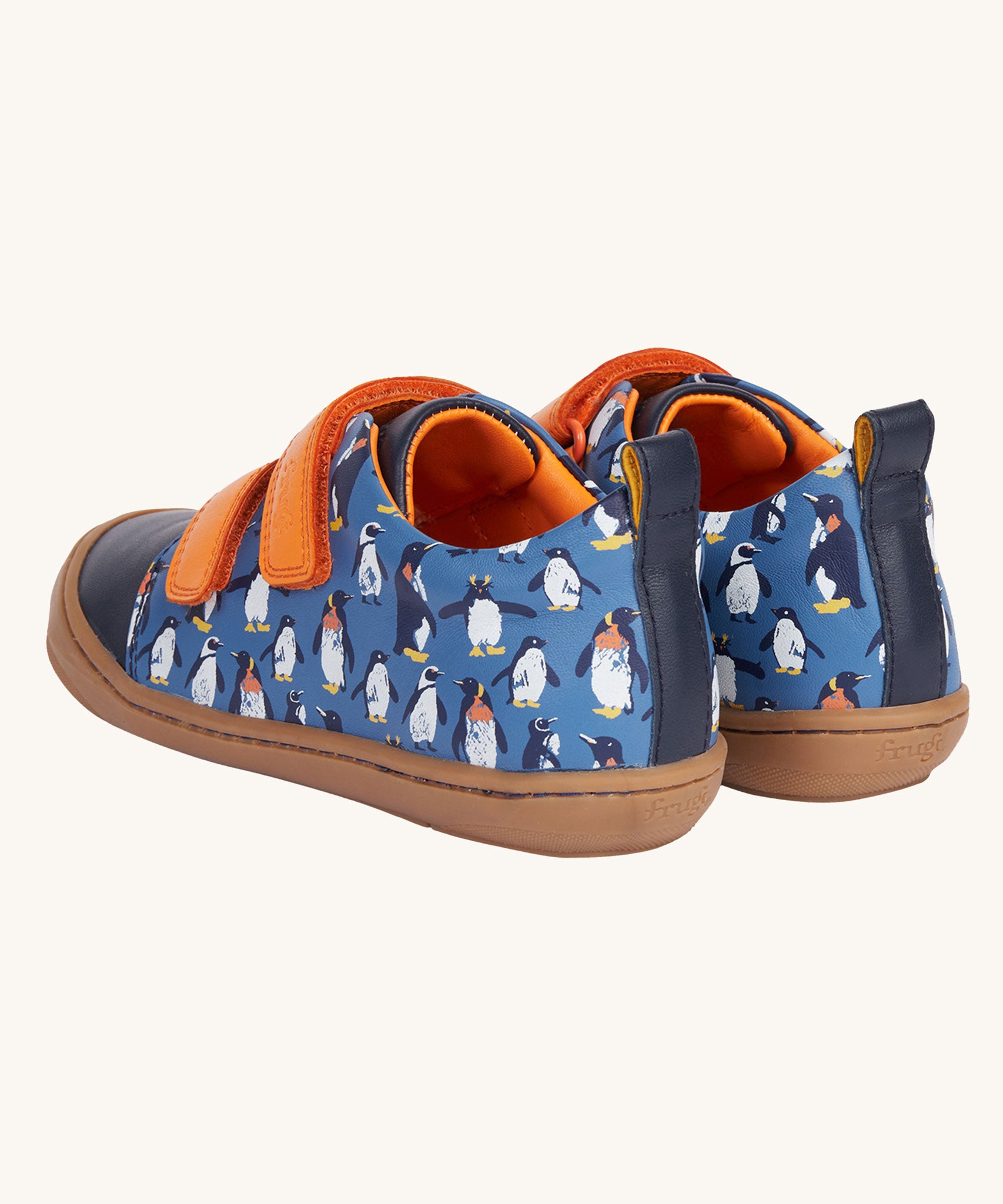 A view of the back of the Frugi Penguin Print Tide Low Top velcro closure leather children's shoes. There is a navy blue strip at the back with a pull tab attached to it for easy on and offs.