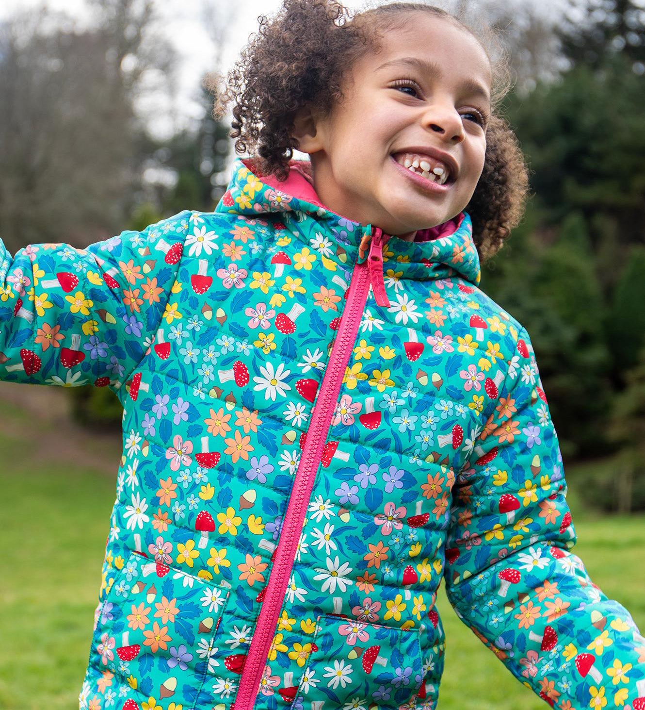 A child wearing the Frugi toasty trail reversible jacket showing the playful woodland inspired design with pink zip detail on post consumer recycled polyester fabric