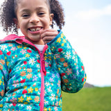 A child wearing the Frugi toasty trail reversible jacket showing the playful woodland inspired design with pink zip detail and light blue trim on the arm on post consumer recycled polyester fabric