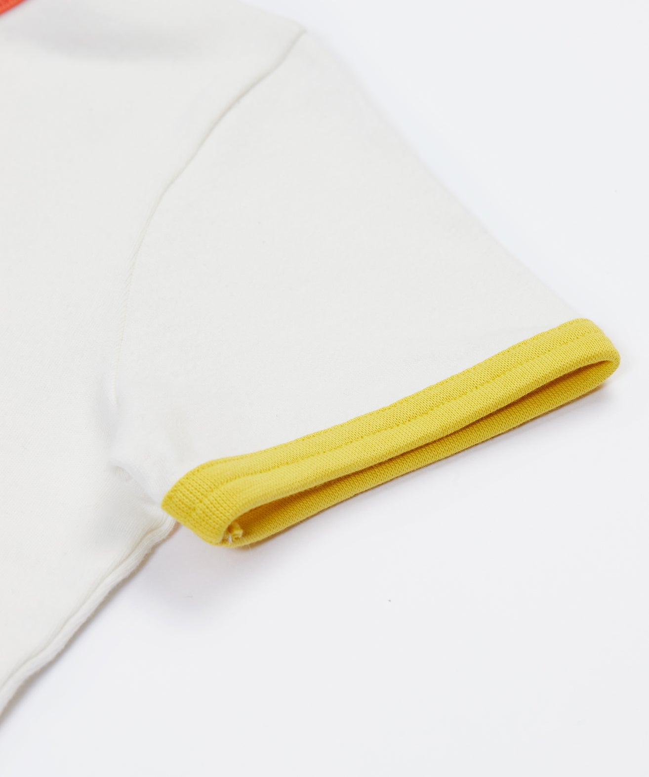 A close up of Frugi Xavier Circus T-Shirt's sleeve, a Soft White t-shirt with a yellow hem detail.