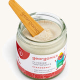 A opened jar of the strawberry fluoride toothpaste with a wooden spatula dipped in.