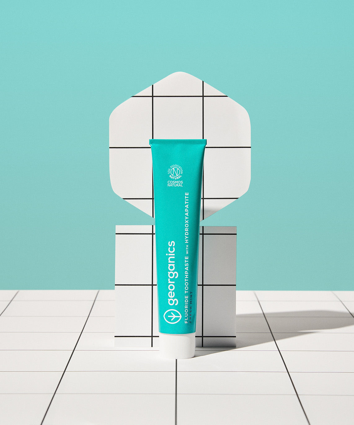 Front view of the Georganics fresh mint hydroxyapatite toothpaste tube on a tile style floor and matching light green background.