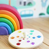 Glückskäfer Fantasy Sparkling Spinning Top placed on a wooden windowsill next to a Grimm's 6 piece rainbow.