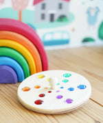 Glückskäfer Fantasy Sparkling Spinning Top placed on a wooden windowsill next to a Grimm's 6 piece rainbow.