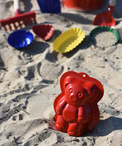 Gluckskafer plastic-free metal teddy bear shaped sand mould toy placed in the sand on a beach.