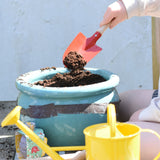 A child using the Glückskäfer Round Metal Red Shovel to place soil into a pot.