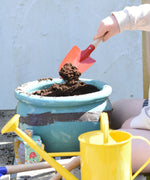 A child using the Glückskäfer Round Metal Red Shovel to place soil into a pot.