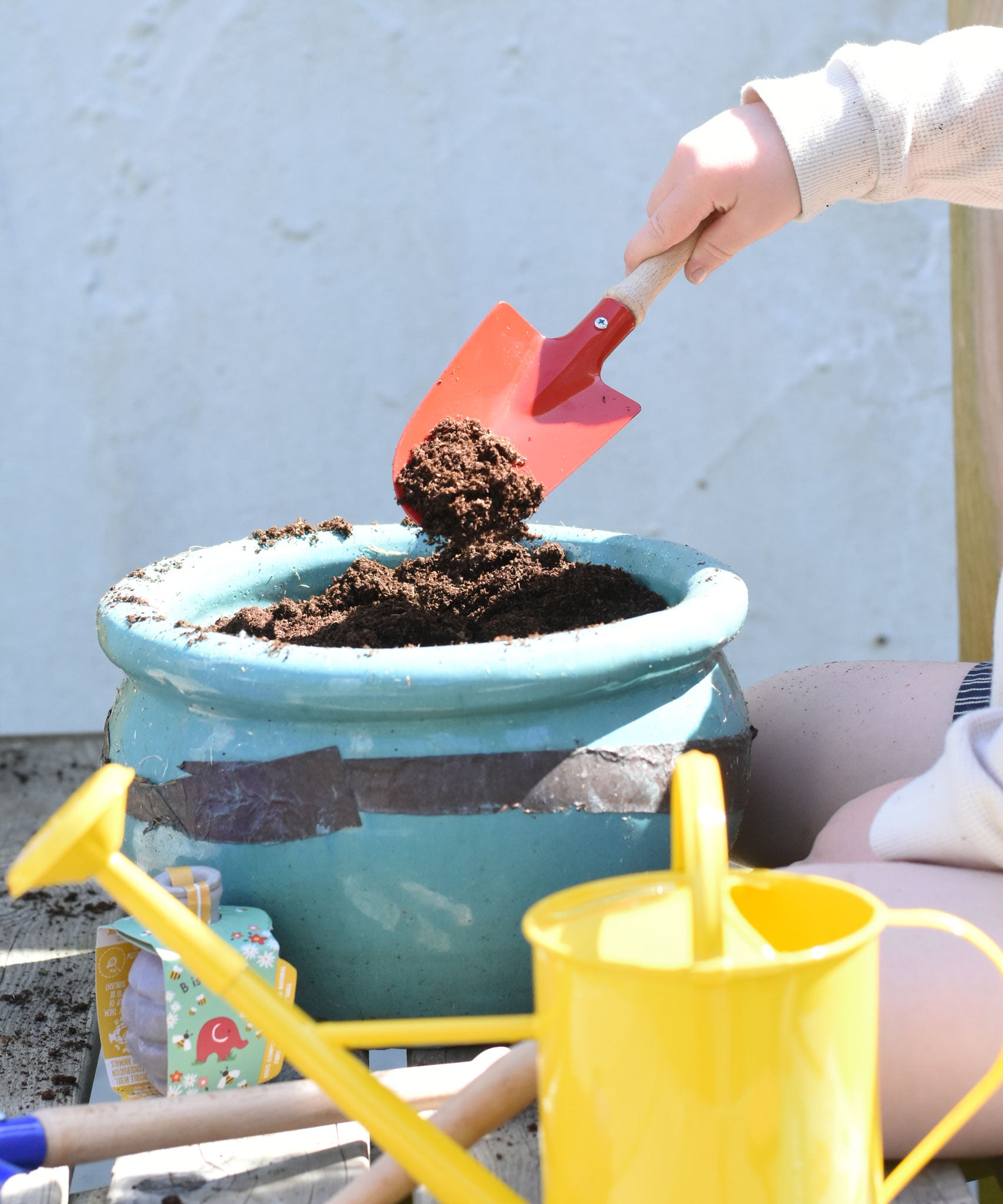 A child using the Glückskäfer Round Metal Red Shovel to place soil into a pot.