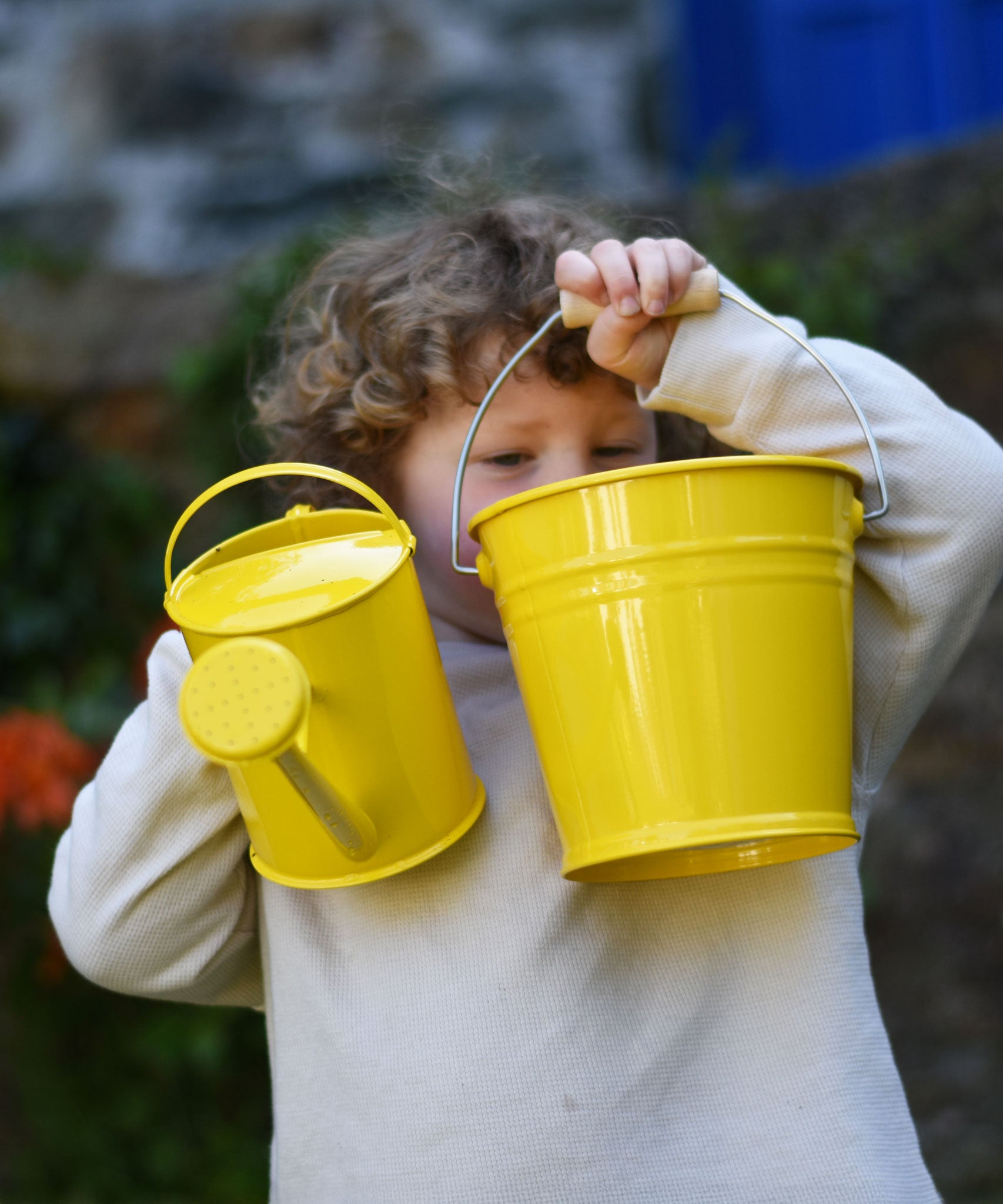 A child holding up a Glückskäfer yellow 1L Metal Watering can and a bucket.