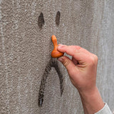 Close up of a child's hand holding up an orange Grapat mandala pumpkin to a sad face