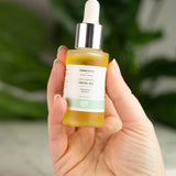 A bottle of Green People Anti-Ageing Facial Oil being held up in a persons hand.