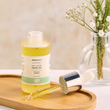 A bottle of Green People Anti-Ageing Facial Oil placed on an oval shaped bamboo dish. The pipette dispenser lid is resting besides the bottle on the dish