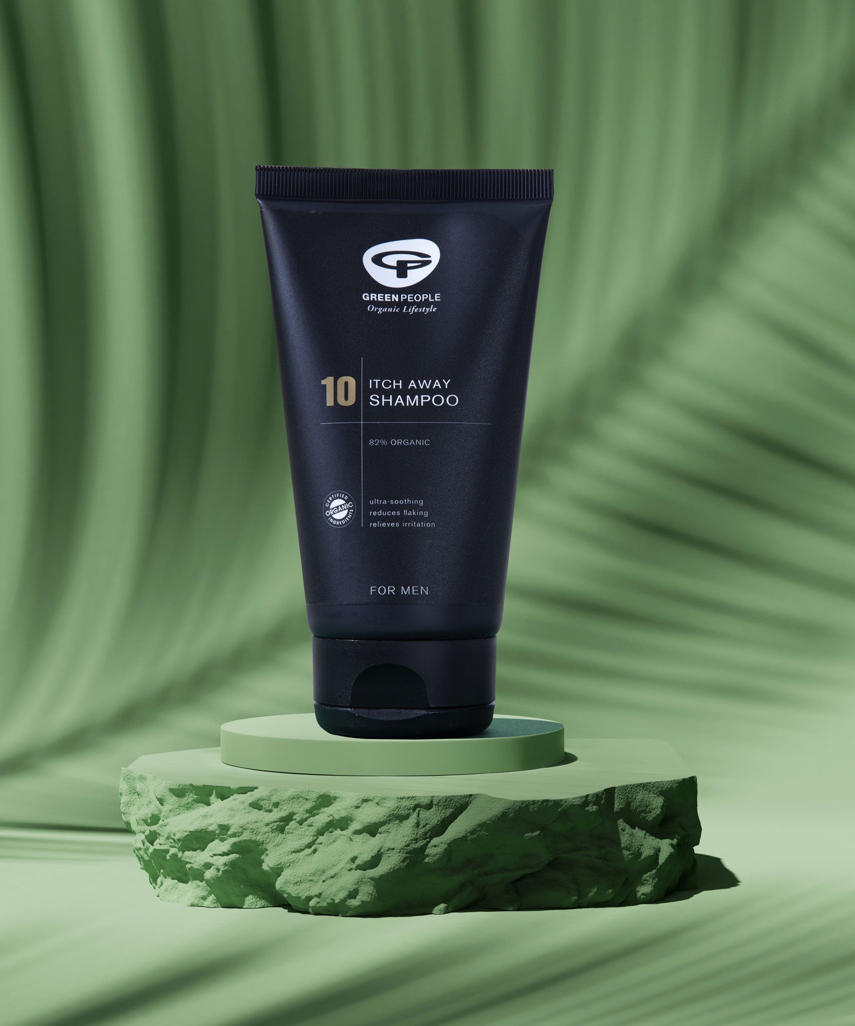 A tube of Green People no.10 Itch Away Shampoo placed on a  green coloured disc pictured against a green background.