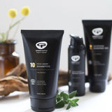 A tube of Green People no.10 Itch Away Shampoo placed on a white surface, there are ither products from the mens collection on the background.