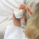 A close up of an adult's hand scooping some product out of the Organic Babies Mum & Baby Rescue Balm pot with their finger.