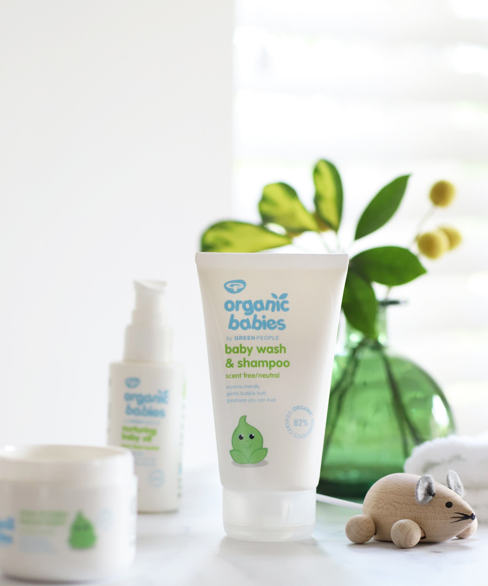 Organic Babies Baby Wash & Shampoo Scent Free placed on a white surface next to a wooden toy mouse. Other products from the organic babies collection can be seen in the background.