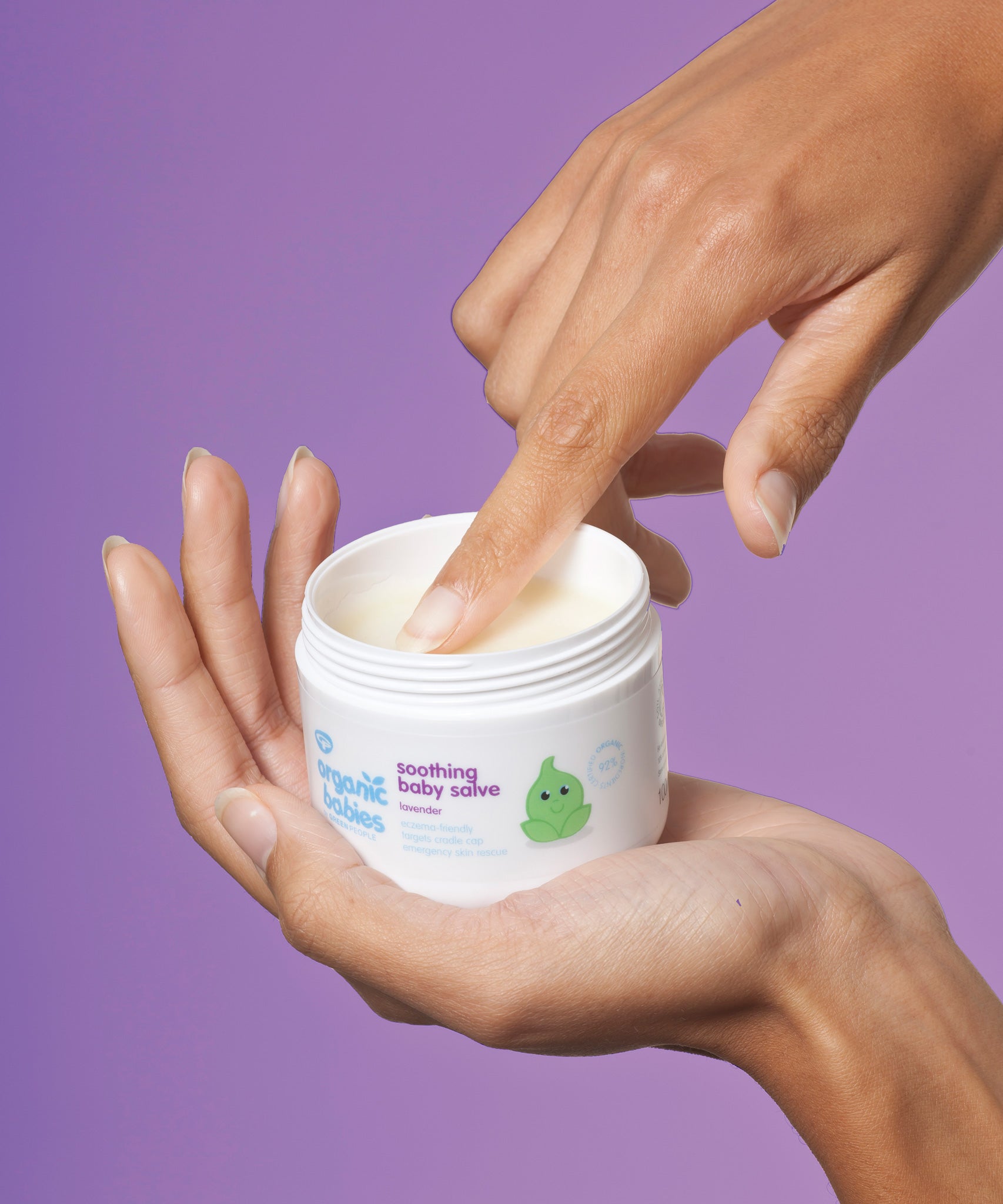Organic Babies Soothing Baby Salve by Green People in a person's palm. The person is scooping some product from the pot with their finger.