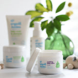 Organic Babies Soothing Baby Salve pictured on a white surface in front of other products from teh organic babies collection.