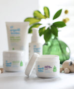 Organic Babies Soothing Baby Salve pictured on a white surface in front of other products from teh organic babies collection.