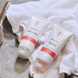 Green People Quinoa & Artichoke protein boost shampoo and conditioner on a white towel. A ceramic pot with a bamboo toothbrush can be seen at the side.