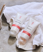 Green People Quinoa & Artichoke protein boost shampoo and conditioner on a white towel. A ceramic pot with a bamboo toothbrush can be seen at the side.