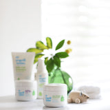 Organic Babies mum & baby Scent Free rescue balm placed on a white surface next to a wooden toy mouse. Other products from the organic babies collection can be seen in the background.