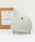 Maël Diffuser, a light grey dome plug-in essential oil diffuser with wooden feet, and cardoard packaging behind.